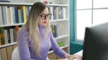 Young blonde woman student using computer studying at library university