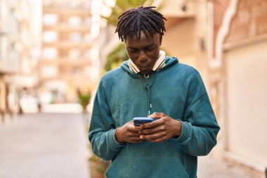 Afro-Amerikalı adam akıllı telefon kullanıyor ve sokakta ciddi bir ifade kullanıyor.