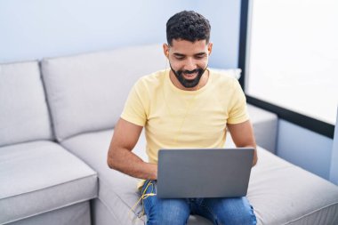 Young arab man using laptop sitting on sofa at home
