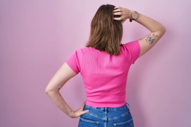 Sarışın, beyaz bir kadın pembe arka planda dikiliyor ve elleri kafasında şüpheyi düşünüyor. 