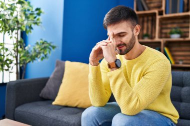 Young hispanic man stressed sitting on sofa at home