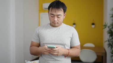Genç Çinli adam evde akıllı telefon kullanıyor.