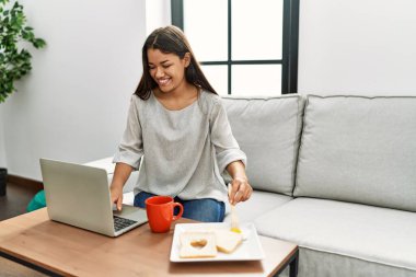 Genç Latin kadın kahvaltısını yapıyor. Evdeki kanepede oturuyor.