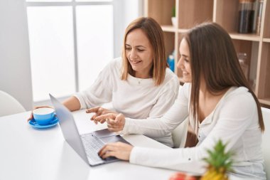 İki kadın anne ve kız evde kahve içerek dizüstü bilgisayar kullanıyorlar.