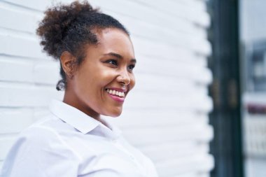 Afro-Amerikalı kadın gülümsüyor. Kendinden emin bir şekilde caddeye bakıyor.