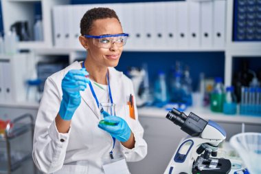 African american woman scientist smiling confident pouring liquid on test tube at laboratory