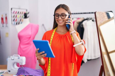 Güzel İspanyol kadın çiçekçi, terzi dükkanında dokunmatik ped kullanarak akıllı telefondan konuşuyor.