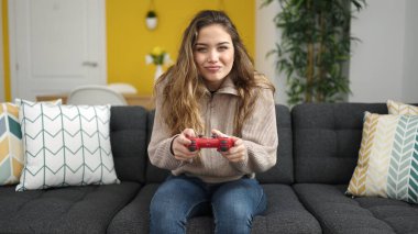 Evdeki kanepede oturmuş video oyunu oynayan genç ve güzel İspanyol kadın.