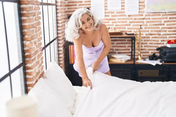 중년의 백발의 여자가 자신있게 침대를정돈하는 미소짓고 있습니다 — 스톡 사진