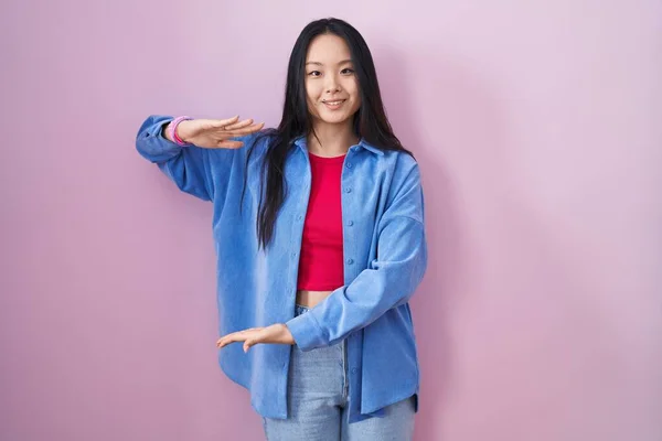 Młoda Azjatka Stojąca Nad Różowym Tłem Gestykulująca Dłońmi Pokazującymi Duży — Zdjęcie stockowe