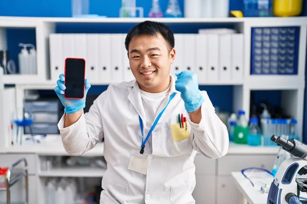 スマートフォンを持っている科学研究所で働いている若い中国人男性は誇りを持って叫んで 勝利と成功を祝う非常に腕を上げ興奮して — ストック写真