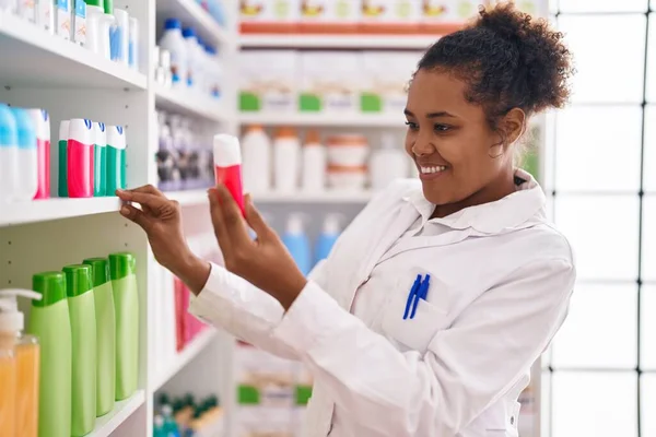 African American Woman Pharmacist Smiling Confident Holding Toothpaste Shelving Pharmacy — Stockfoto