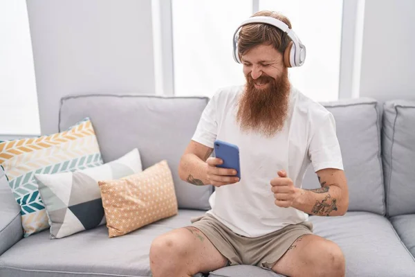 Young Redhead Man Listening Music Sitting Sofa Home — Stockfoto