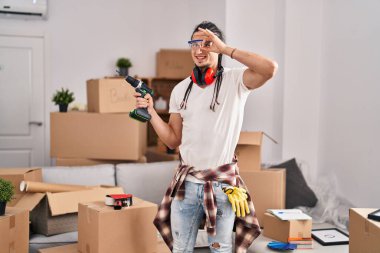 Yeni evinde elinde tornavida tutan uzun saçlı İspanyol bir adam gülümsüyor. 