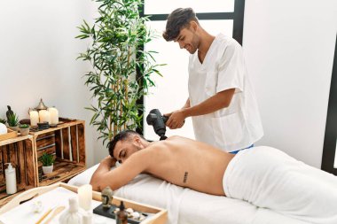 İki İspanyol fizyoterapist ve hasta güzellik merkezinde perküsyon silahı kullanarak masaj yapıyorlar.