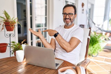 Orta yaşlı bir adam evde bilgisayarını kullanırken kameraya hayret ediyor ve gülümsüyor.. 