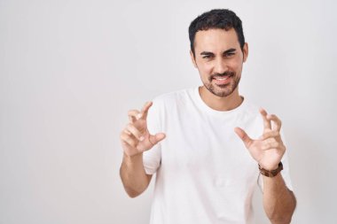 Beyaz arka planda duran yakışıklı İspanyol adam komik bir şekilde kedi gibi gülüyor, agresif ve seksi bir ifade takınıyor. 