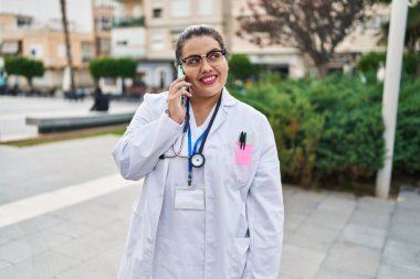 Young beautiful plus size woman doctor smiling confident talking on smartphone at park