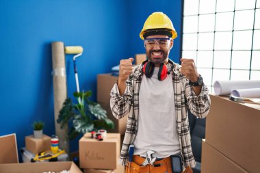 Evde sakallı genç İspanyol bir adam başarılı olacağı için heyecanlı kolları havada ve gözleri kapalı zaferi kutlarken gülümsüyor. Kazanan konsept. 