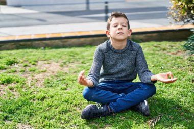 Sarışın çocuk parkta çimlerin üzerinde yoga egzersizi yapıyor.