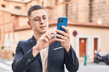 Young hispanic man executive smiling confident using smartphone at street