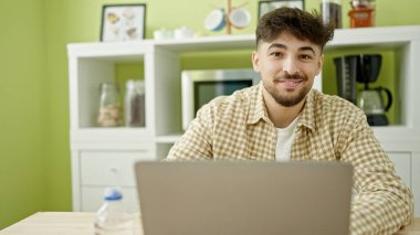 Genç Arap adam evdeki masada dizüstü bilgisayar kullanıyor.