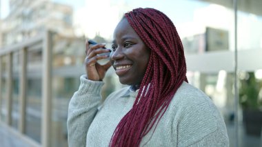 Örgülü saçlı Afrikalı bir kadın sokakta akıllı telefonuyla sesli mesaj dinliyor.