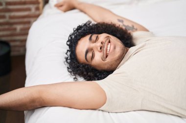 Genç latin adam yatak odasında kollarını esneterek uyanıyor.