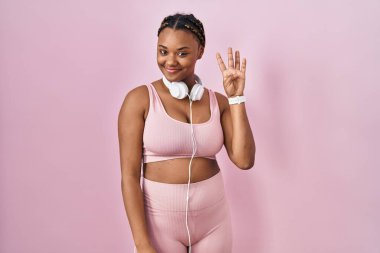Spor kıyafetleri ve kulaklıkları takan Afro-Amerikalı kadın dört numarayı gösterip işaret ederken kendine güvenen ve mutlu gülümseyen.. 