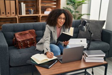 Young african american woman psychologist using laptop and writing book at psychology center