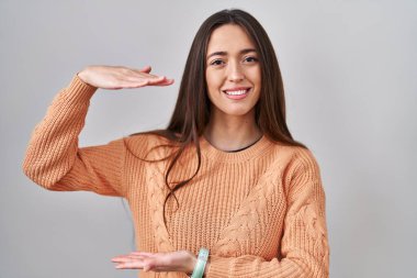 Beyaz arka planda duran esmer bir kadın. Ellerinde büyük ve büyük bir işaret, ölçü sembolü var. Kameraya bakıp gülümsüyor. ölçüm kavramı. 