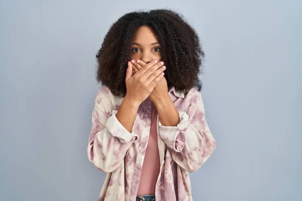 青い背景の上に立っている若いアフリカ系アメリカ人の女性は間違いのために手で口をカバーショックを受けた 秘密の概念 — ストック写真