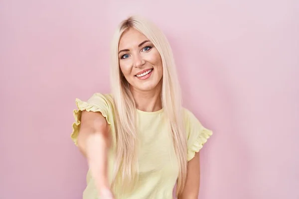 stock image Caucasian woman standing over pink background smiling friendly offering handshake as greeting and welcoming. successful business. 