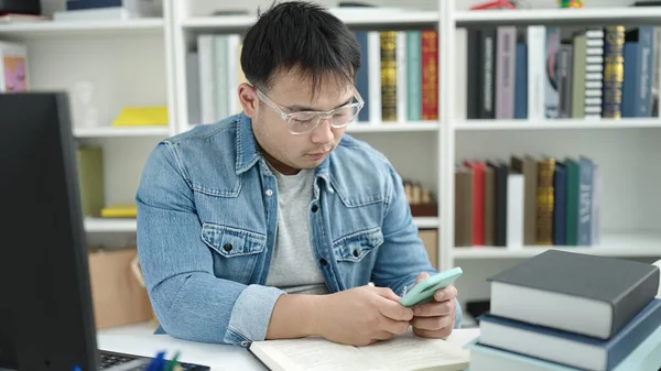 Młody Chiński Człowiek Student Pomocą Smartfona Siedzi Stole Uniwersytecie Biblioteki — Zdjęcie stockowe