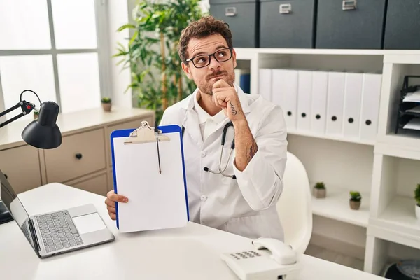 Young Hispanic Man Wearing Doctor Stethoscope Holding Clipboard Serious Face — Stock Photo, Image