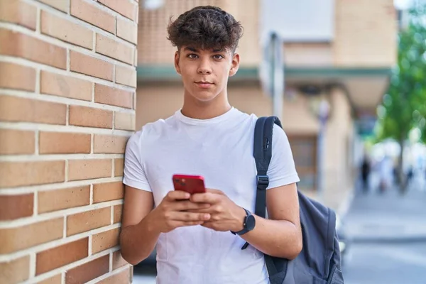 ストリートでリラックスした表情のスマートフォンを使用して若いヒスパニック系のティーンエイジャーの学生 — ストック写真