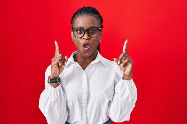 Kırmızı arka planda dikilen örgü ören Afrikalı kadın şaşırmış ve şaşırmış bir şekilde yukarı bakıp parmaklarını göstermiş ve kollarını kaldırmıştı.. 