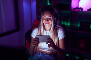 Young beautiful hispanic woman streamer playing video game using smartphone at gaming room