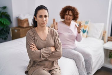 Two women mother and daughter arguing sitting on bed 