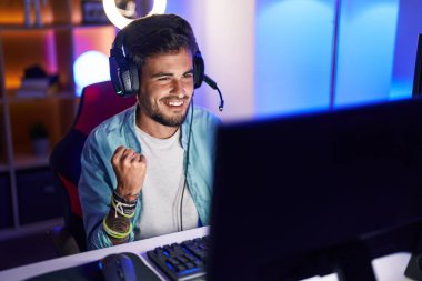 Oyun odasında İspanyol asıllı genç adam video oyunu oynuyor.