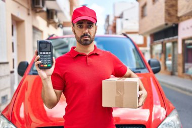 Sakallı, teslimat üniforması giyen, elinde veri bankası tutan, kuşkucu ve gergin bir İspanyol genç, sorun yüzünden surat asıyor. negatif kişi. 