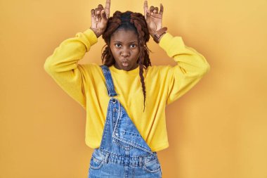Sarı arka planda dikilen Afrikalı kadın boynuz gibi parmaklarıyla komik hareketler yapıyor. 