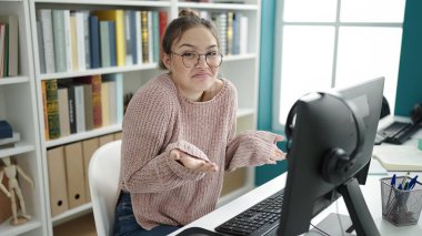 Young beautiful hispanic woman student using computer doing i dont know gesture at library university