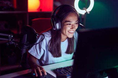 Young beautiful hispanic woman streamer playing video game using computer at gaming room