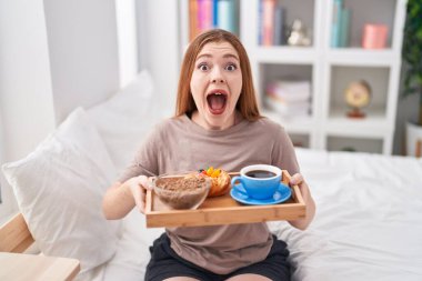 Pijama giyen kızıl saçlı kadın kahvaltı tepsisini tutarak çılgın ve başarıyı kutlarken gözleri açık heyecanla haykırıyor.. 