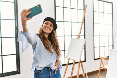 Genç ve güzel İspanyol kadın sanatçı sanat stüdyosunda akıllı telefonla selfie çekiyor.