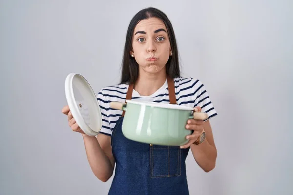 Young Brunette Woman Wearing Apron Holding Cooking Pot Puffing Cheeks — Stock Photo, Image