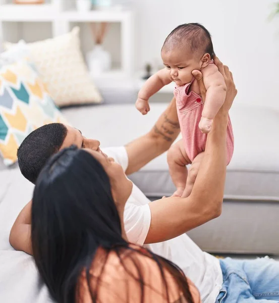 Hispanic family holding baby on air sitting on floor at home