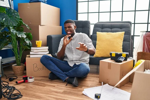 African american man sitting on the floor at new home disgusted expression, displeased and fearful doing disgust face because aversion reaction.