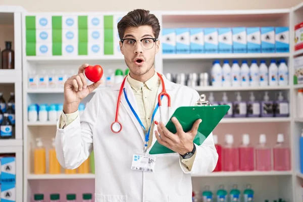Young Hispanic Man Working Pharmacy Drugstore Holding Heart Afraid Shocked — Zdjęcie stockowe
